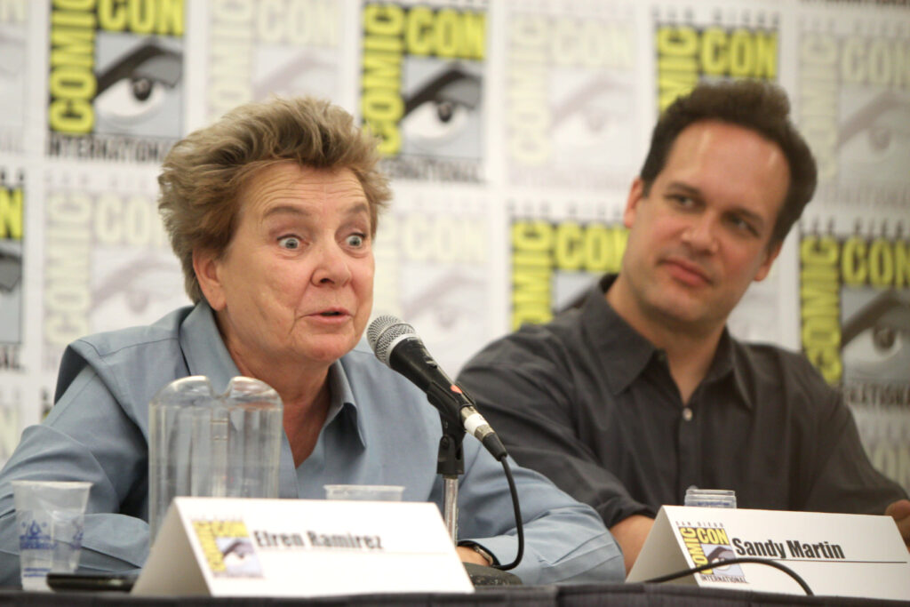 Actress Sandy Martin speaking animatedly at Comic-Con panel with Diedrich Bader seated beside her Wallpaper