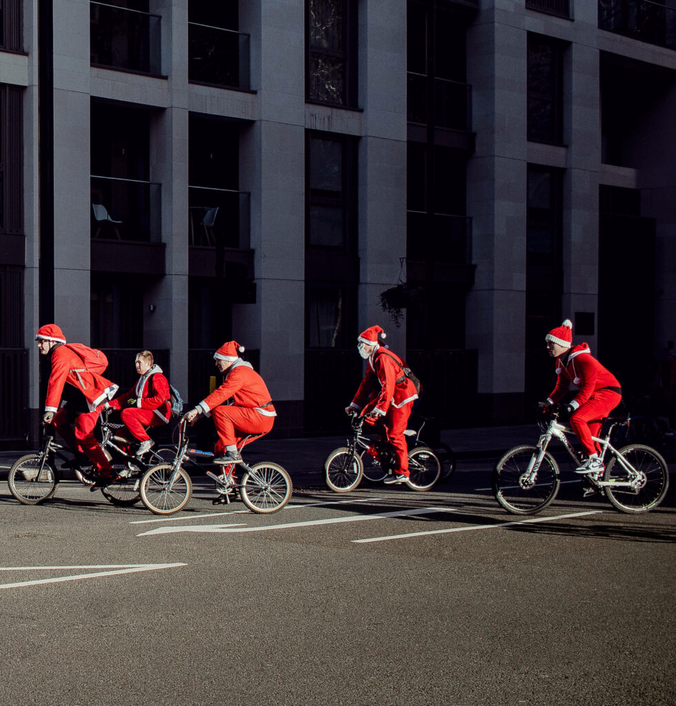 Santa Claus biking with friends in festive city scene enjoying a playful breezy holiday ride Wallpaper