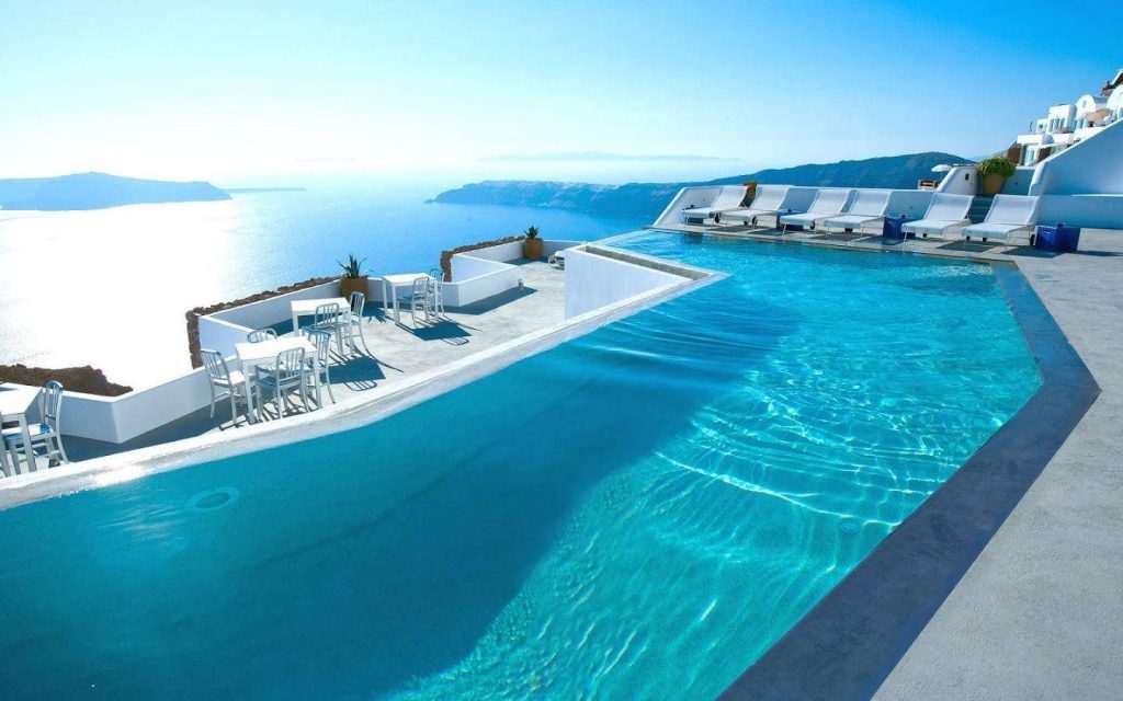 Infinity pool with white Santorini cliffs and sparkling Aegean Sea under sunny sky Wallpaper