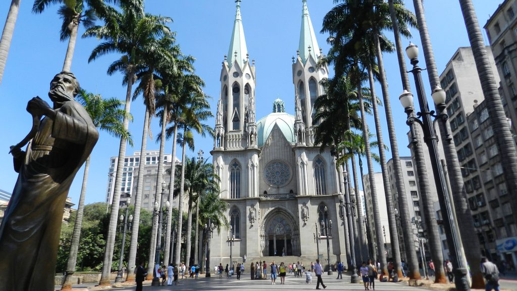 Neo-Gothic São Paulo Cathedral with palm trees and bronze statue under blue sky in city square Wallpaper