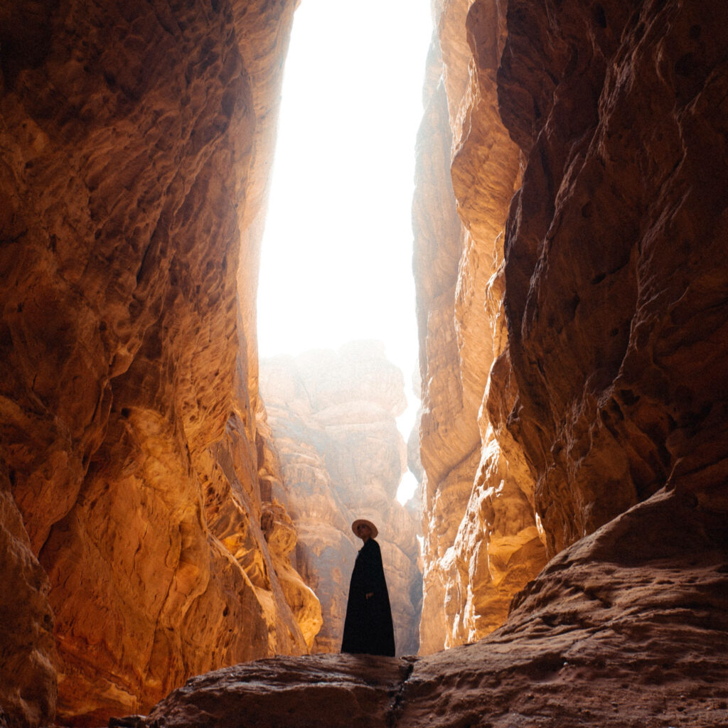 Exploring the Mesmerizing Depths: A Tourist's Journey in a Majestic Saudi Arabian Cave with Black Attire and a Straw Hat Wallpaper