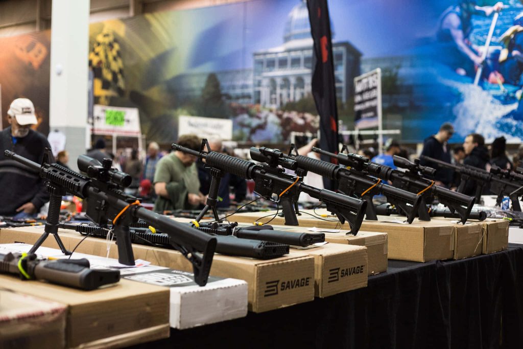 Savage Arms tactical rifles with optics and bipods displayed at a busy trade show wallpaper