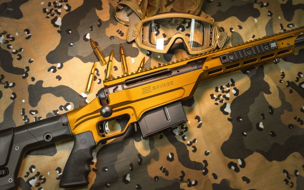 Savage bolt-action rifle with gold chassis brass cartridges tactical goggles camouflage background Wallpaper