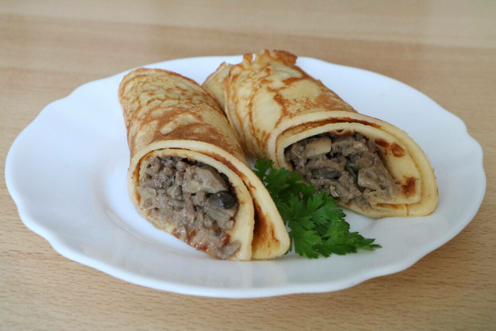 Two roti meat burritos with minced meat mushrooms and cilantro on white plate wooden background Wallpaper