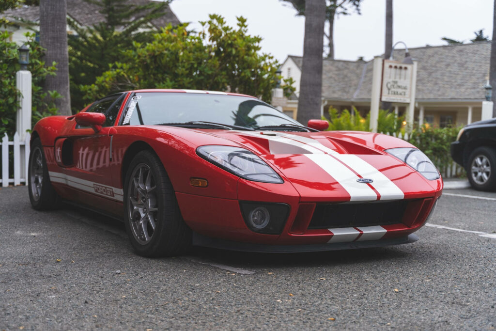 Scarlet Ford GT sports car with white racing stripes parked in scenic outdoor wallpaper background