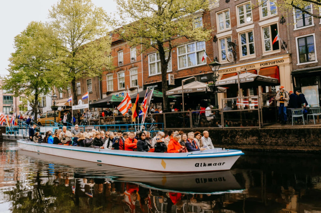 Group enjoying scenic boat ride on Alkmaar canal past historic Dutch buildings and cafes Wallpaper