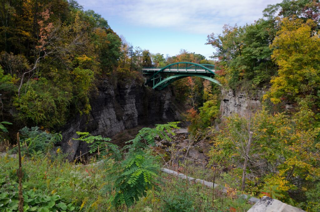 Scenic landscape with autumn trees rocky cliffs and metal bridge under partly cloudy sky wallpaper
