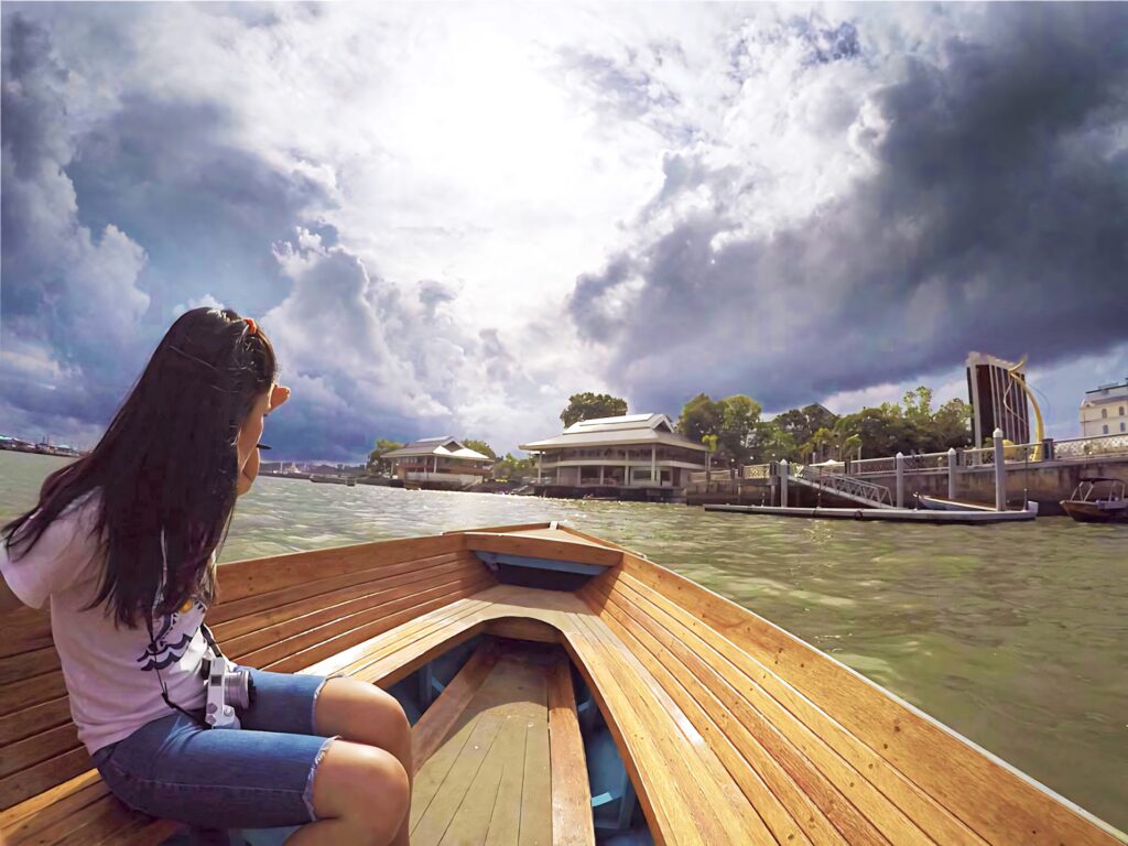 Tourist on boat ride in Brunei waterfront admiring architecture lush greenery and cloudy sky Wallpaper