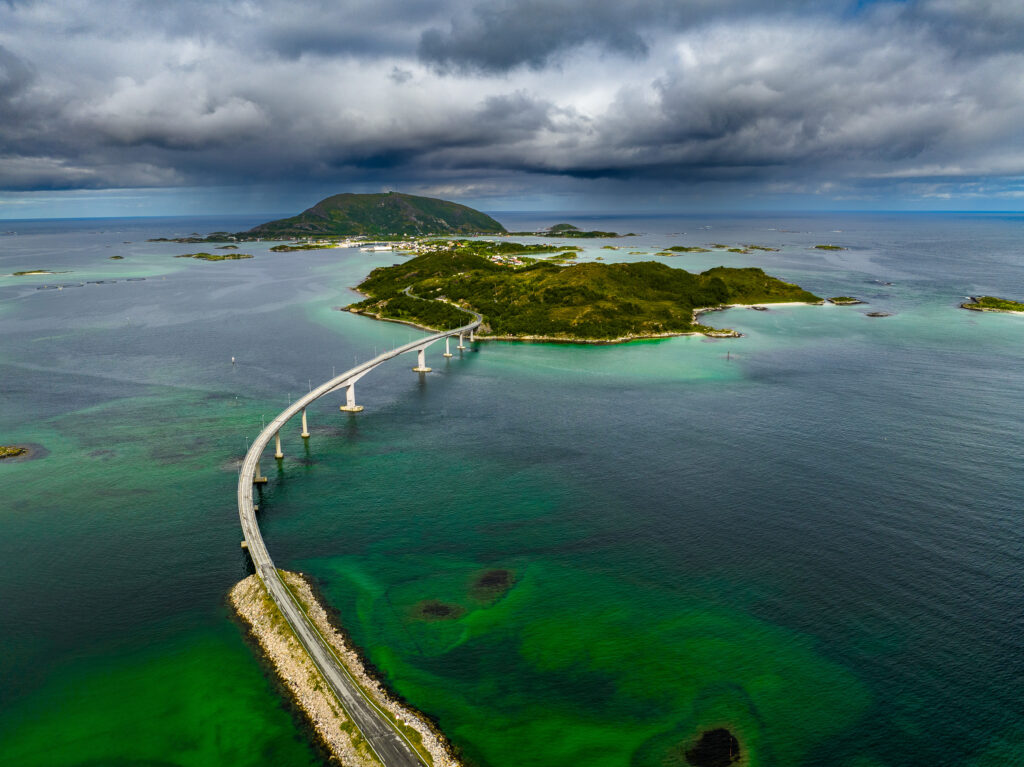 Scenic curved bridge over vibrant green and blue waters connecting lush islands under moody sky Wallpaper
