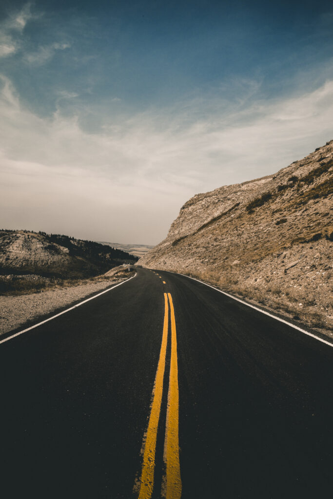 Scenic Montana highway winding through rugged hills with vivid yellow road markings under dramatic sky Wallpaper
