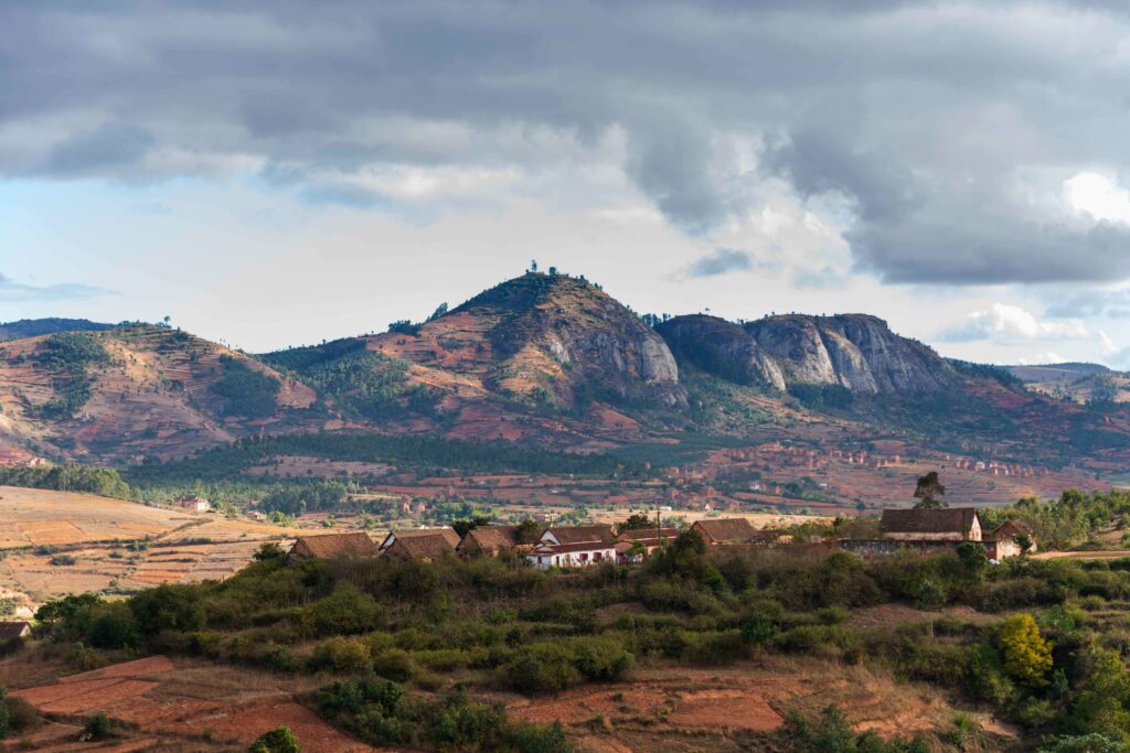 Scenic hillside wallpaper with lush greenery rustic buildings dramatic mountains and cloudy sky