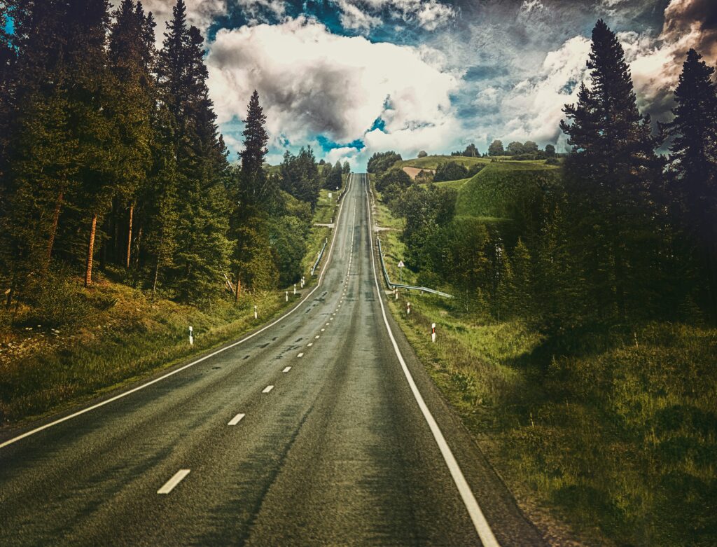 Scenic open road through green trees under dramatic summer sky vibrant adventure wallpaper background
