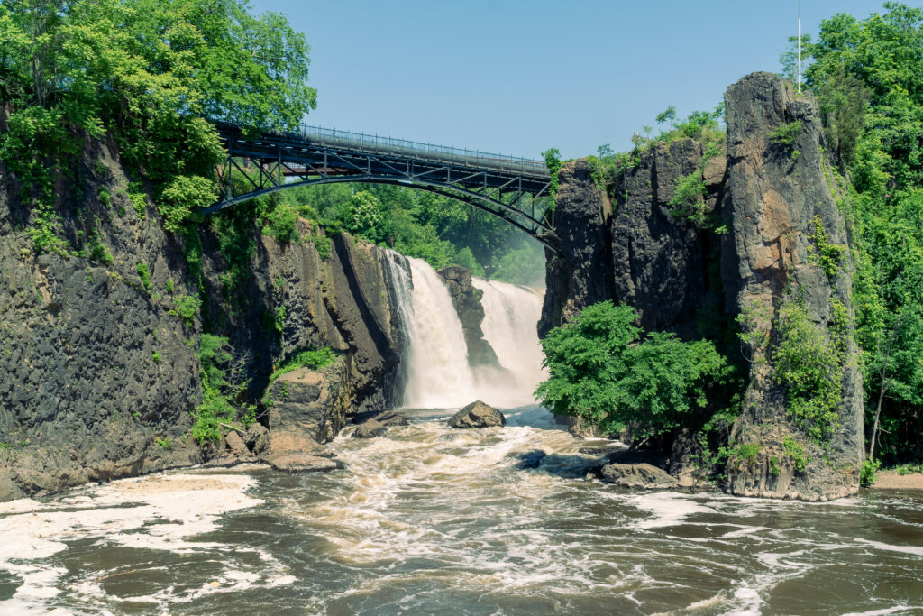 Scenic steel bridge over green cliffs with waterfall and river under bright blue sky wallpaper