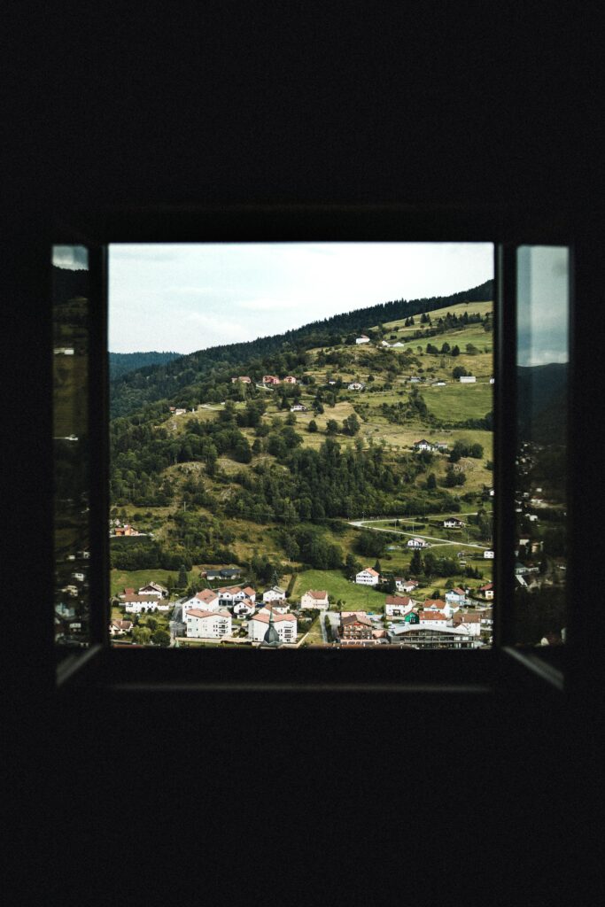 Scenic hillside village view through open window with lush greenery and serene architecture background Wallpaper