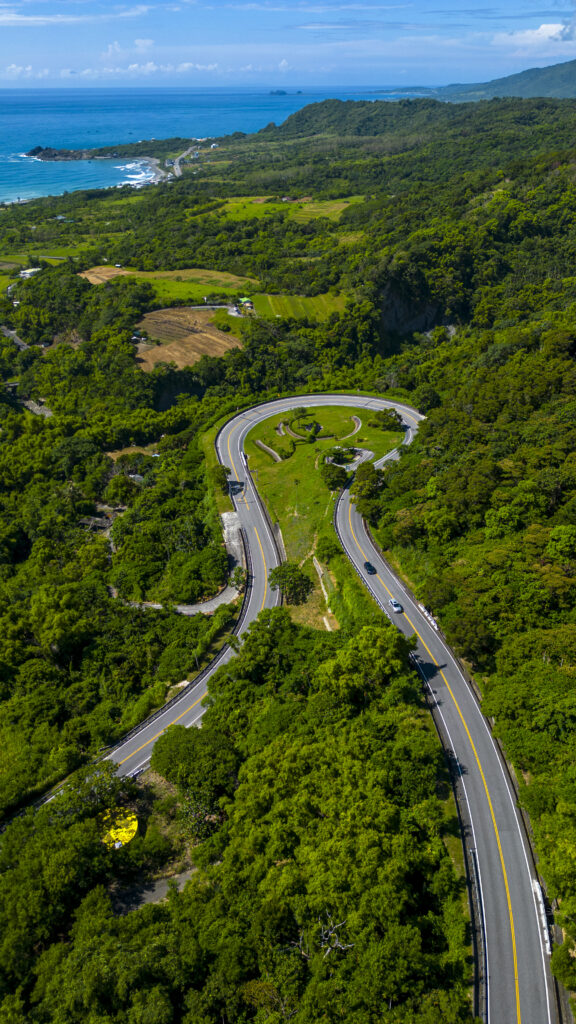 Winding coastal road through lush green trees with blue sea and clear sky scenic wallpaper background