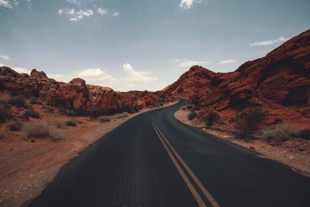 Winding asphalt road with yellow lines through red rocks and dry prairie under clear blue sky Wallpaper
