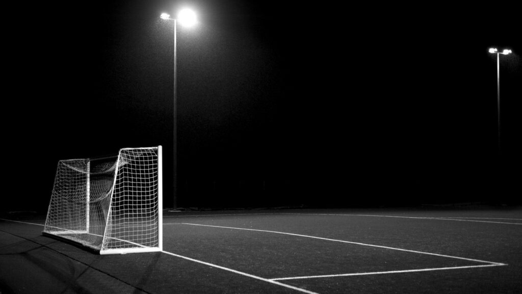 High contrast grayscale soccer goal at night with illuminated net and bright pitch lines background Wallpaper