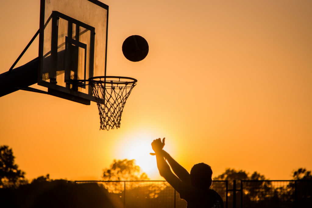 Basketball player silhouette shooting at sunset with glowing orange sky vibrant sports wallpaper