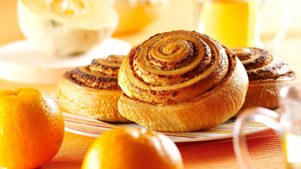 Close-up of golden cinnamon buns with bright oranges and cantaloupe in cozy breakfast scene Wallpaper