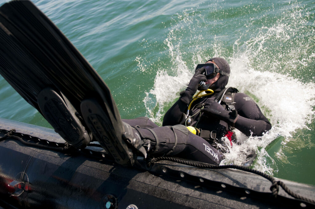 Scuba diver in full gear performing backward roll entry into clear blue water from boat background Wallpaper