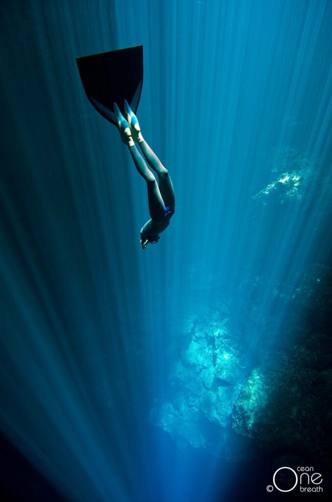 Scuba diver descending into deep blue ocean with sunlight rays and vibrant underwater scenery Wallpaper