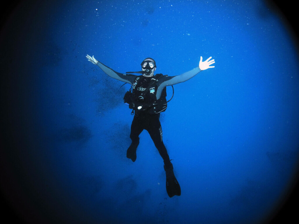 Scuba diver with open arms floats in clear blue ocean bubbles underwater adventure wallpaper