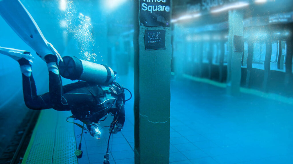 Scuba diver explores flooded Times Square subway station underwater with blue light and urban ruins Wallpaper