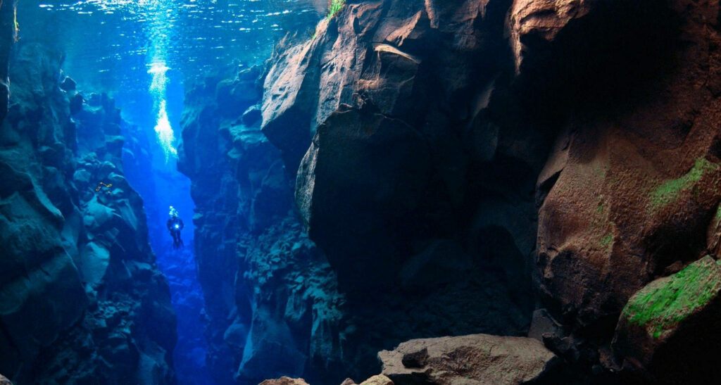 Scuba diver exploring crystal-clear blue Silfra waters between volcanic rock rift background Wallpaper