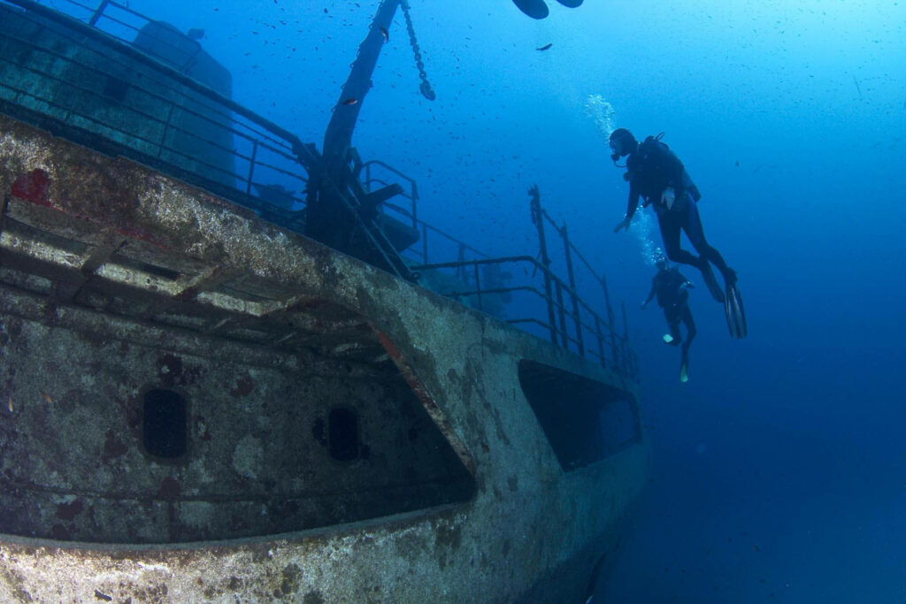 Scuba divers explore sunken shipwreck in deep blue ocean with sunlight and bubbles background wallpaper