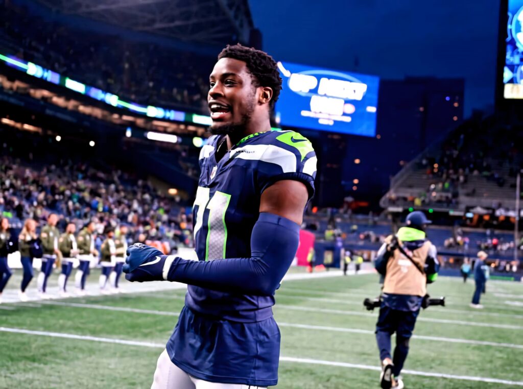 Seahawks Devon Witherspoon smiling on field in navy blue neon green uniform stadium lights crowd Wallpaper