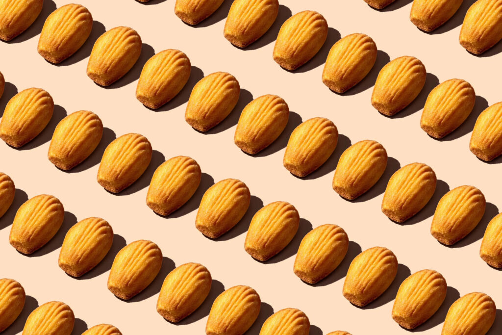 Seamless pattern of golden madeleine cookies arranged diagonally on beige kitchen wallpaper background