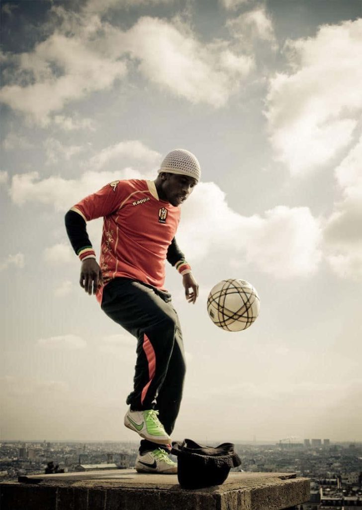 Sean Garnier freestyle football tricks on city rooftop in red Kappa kit with cloudy sky background Wallpaper