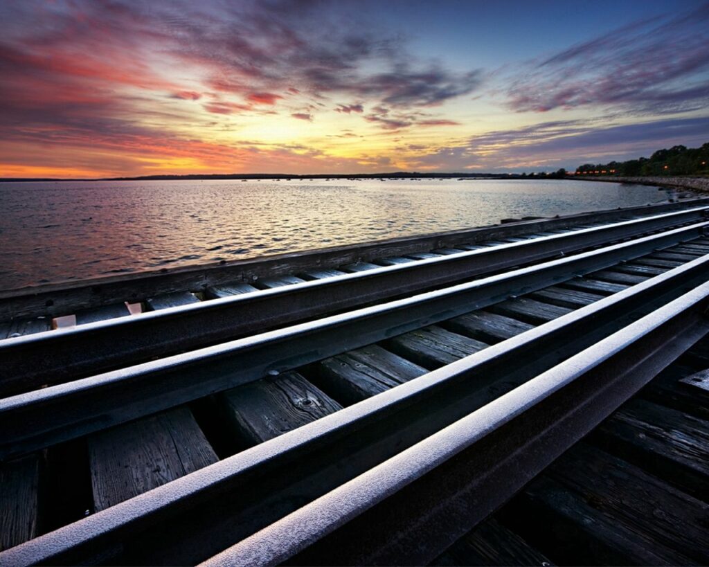 Metal railway tracks along serene seaside with colorful dramatic sunset sky and tranquil water Wallpaper