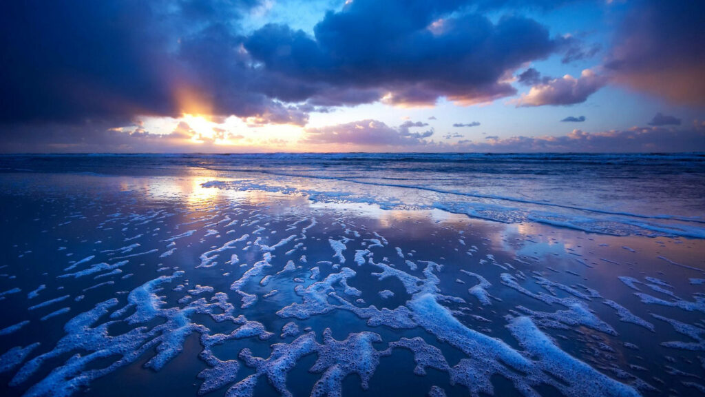 Mesmerizing seaside sunset with golden light and blue clouds over a peaceful beach landscape Wallpaper