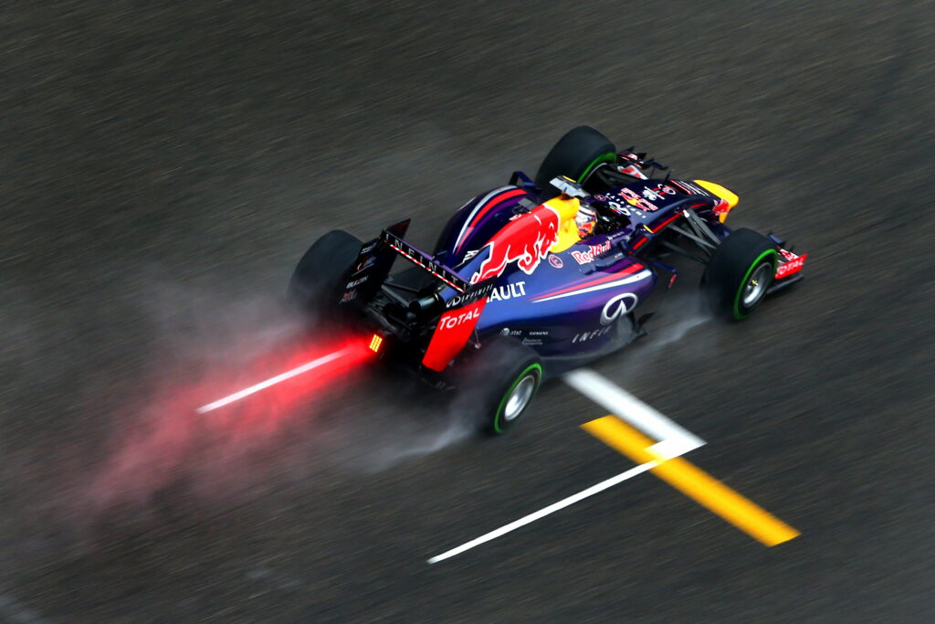 High-angle view of Sebastian Vettel's Red Bull Racing RB10 on wet track with glowing rain light Wallpaper