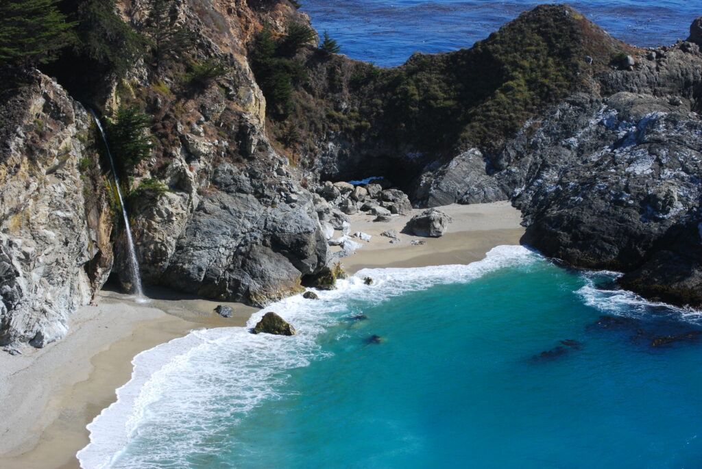 Secluded beach cove with turquoise lagoon rocky cliffs waterfall and soft sandy shore wallpaper