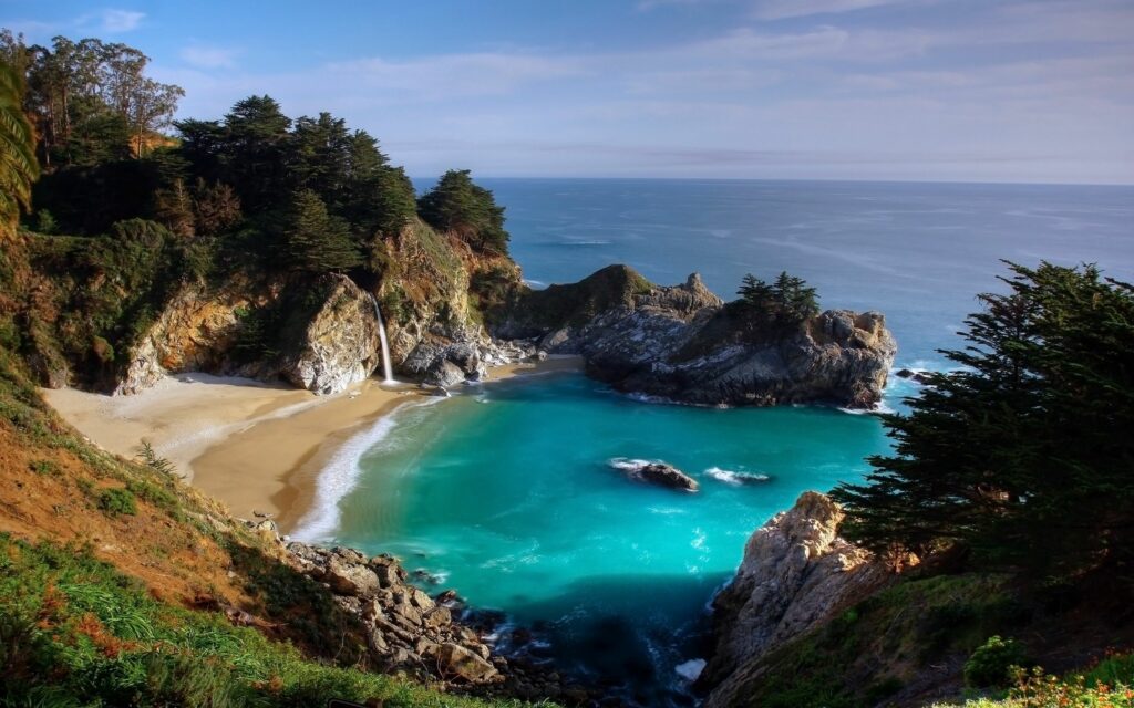 Secluded tropical bay with gentle waterfall sandy beach and vivid turquoise blue water wallpaper