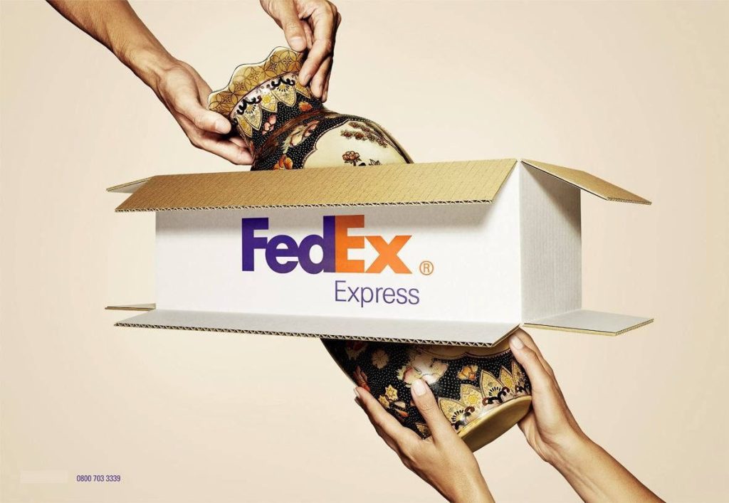 Hands placing ornate black and gold vase into FedEx Express box showcasing secure shipping care Wallpaper