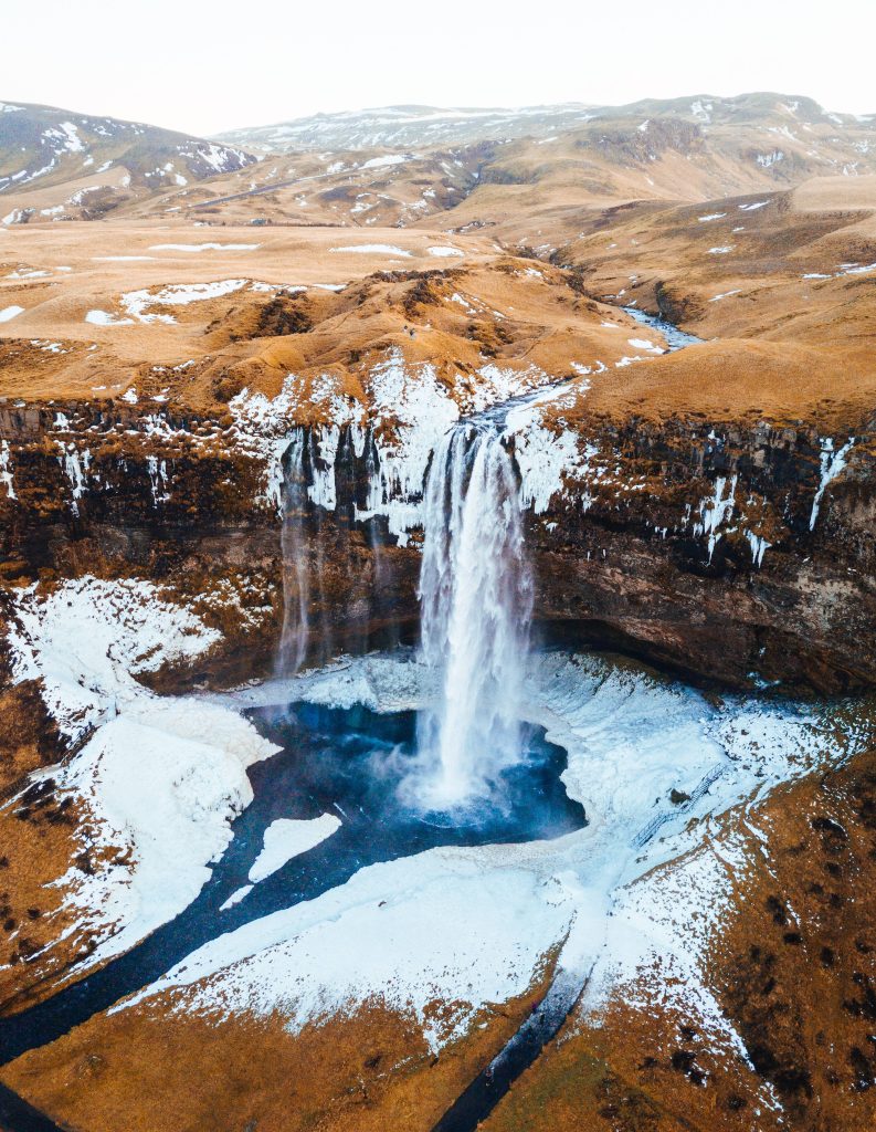 Aerial view of Iceland Seljalandsfoss waterfall flowing into blue pool with snowy cliffs winter Wallpaper