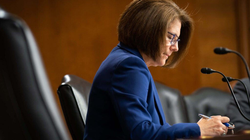 U.S. Senator Catherine Cortez Masto speaking in formal setting with warm brown wallpaper background
