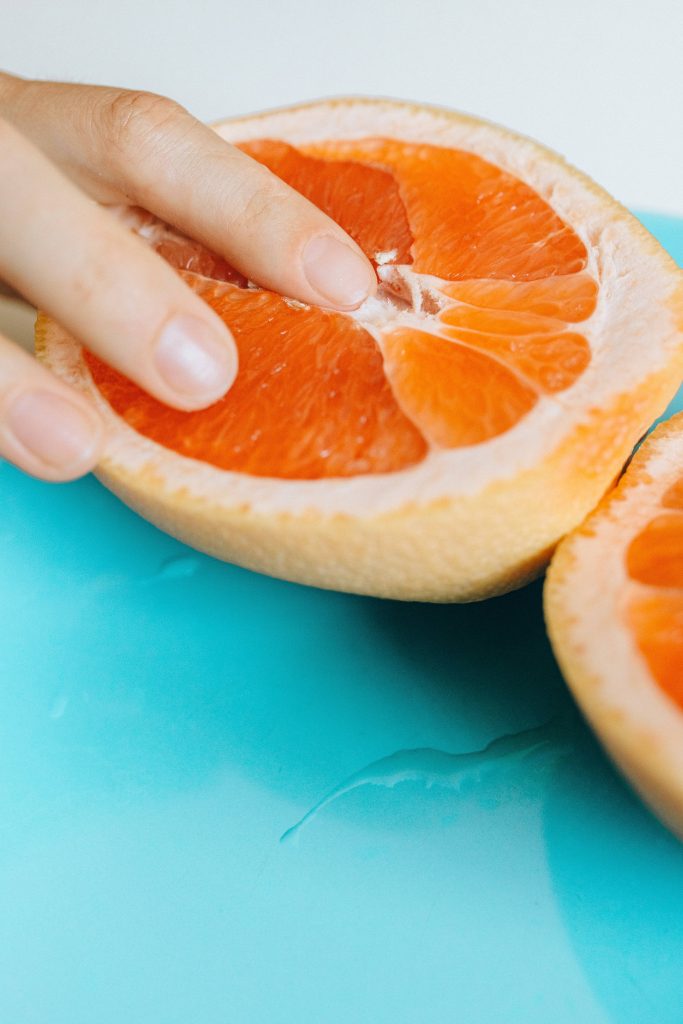 Close-up of hand pressing pink grapefruit half with water droplets on cyan blue background wallpaper