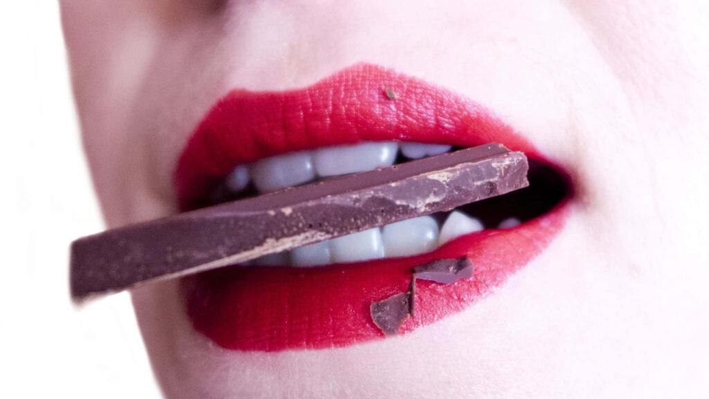 Close up of vibrant red lips biting dark chocolate bar rich contrast modern stylish wallpaper