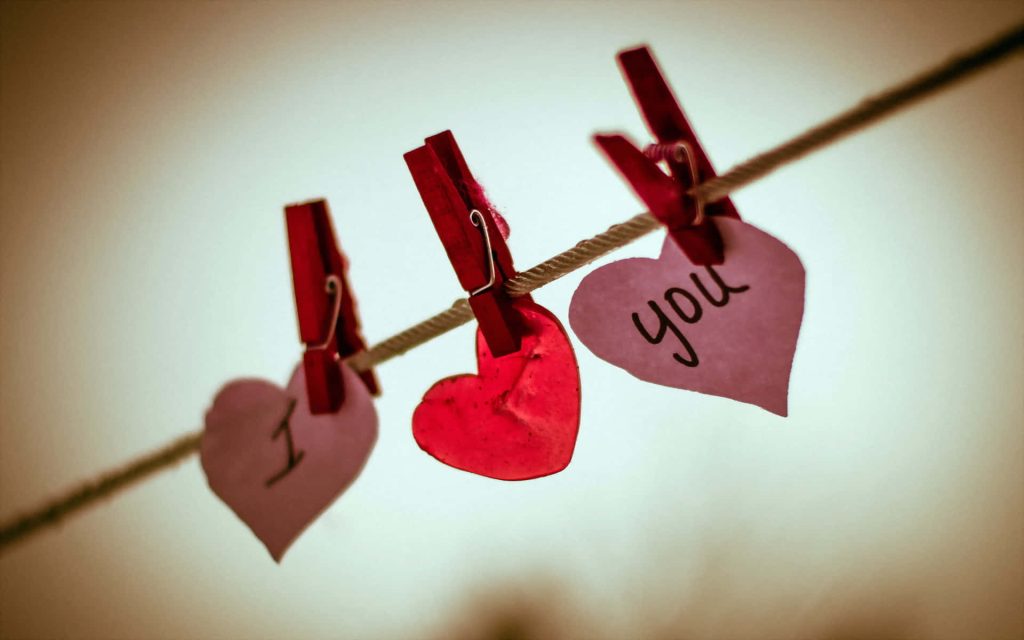 Heart-shaped cutouts spelling I Love You hung on string with red clips romantic background Wallpaper