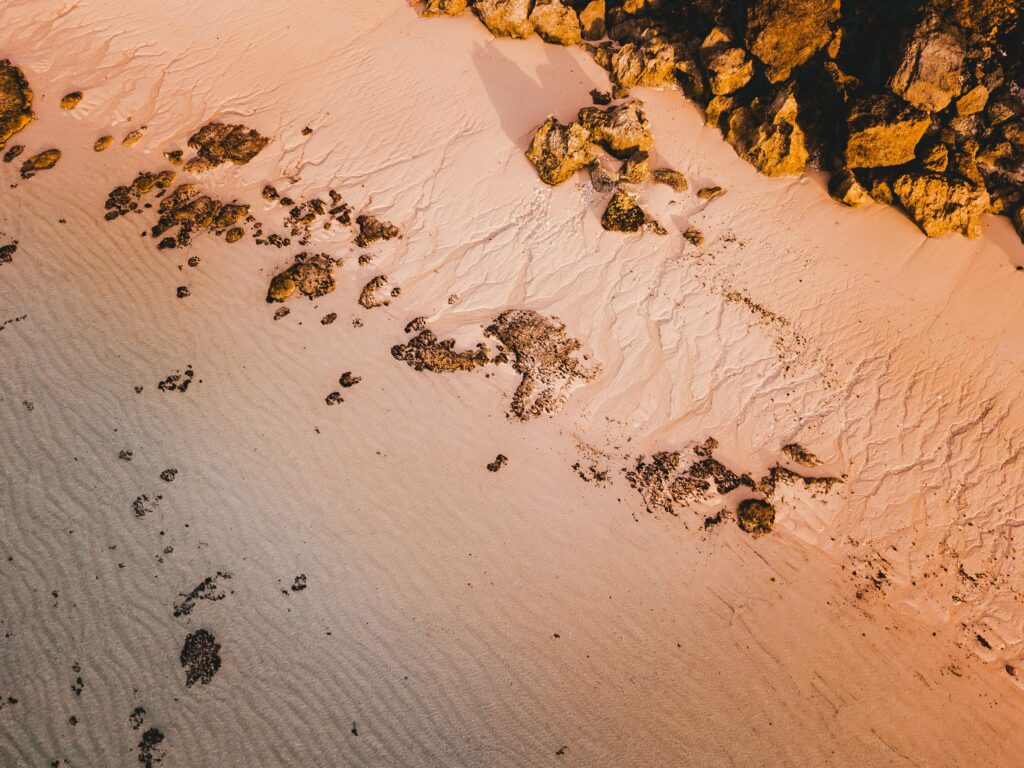 Aerial view of tranquil sandy beach with scattered rocks and warm sunlight coastal wallpaper background