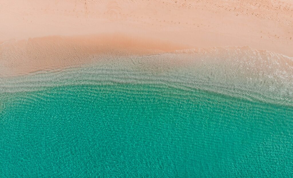 Aerial view of serene beach with turquoise water gently meeting smooth light sandy shore wallpaper