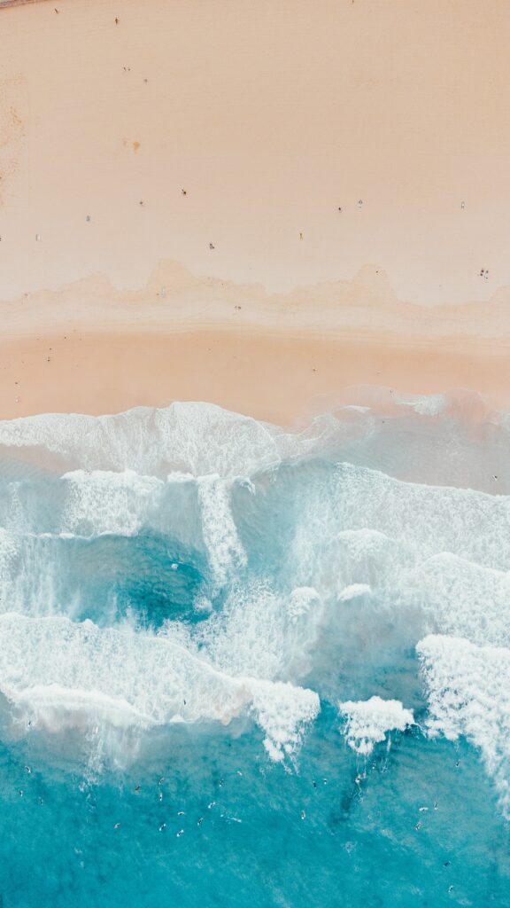 Aerial view of turquoise sea meeting golden sandy beach with small people along shore wallpaper