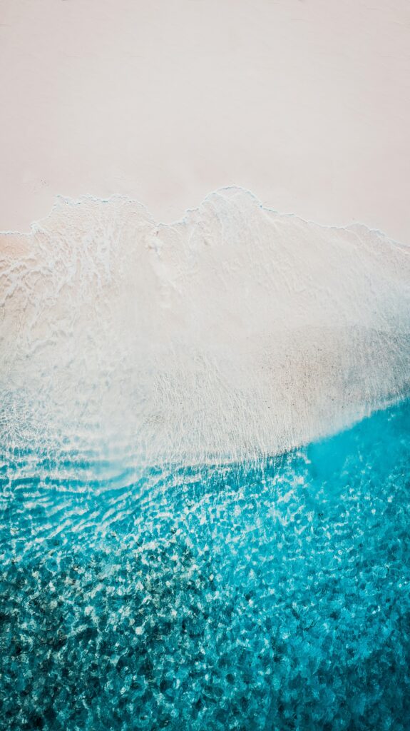 Aerial view of serene sandy beach meeting vibrant blue ocean with gentle textured waves wallpaper
