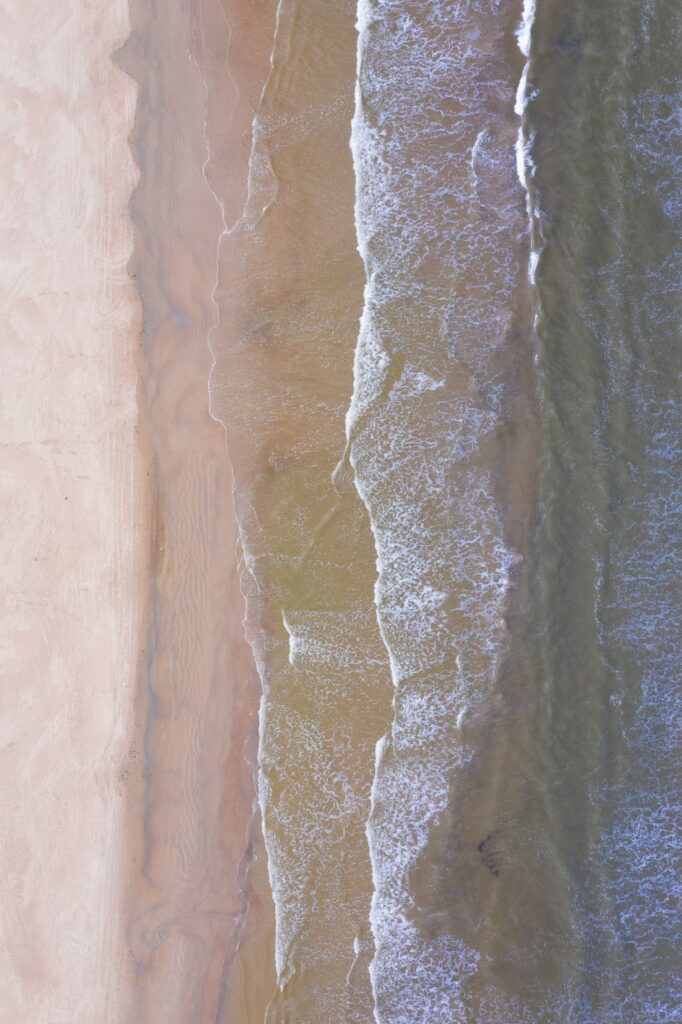Aerial view of serene beach coastline with gentle tide and sandy shore in soft tan and blue hues Wallpaper