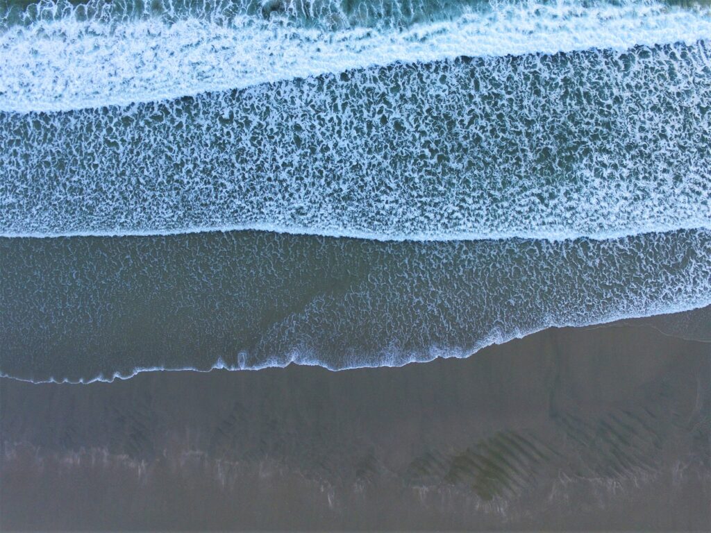 Aerial view of serene beach with rolling waves foamy surf and sandy coastline wallpaper background