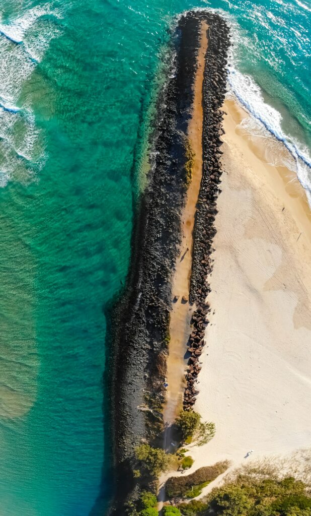 Aerial view of turquoise waves crashing on pebble shore with sandy beach coastal wallpaper
